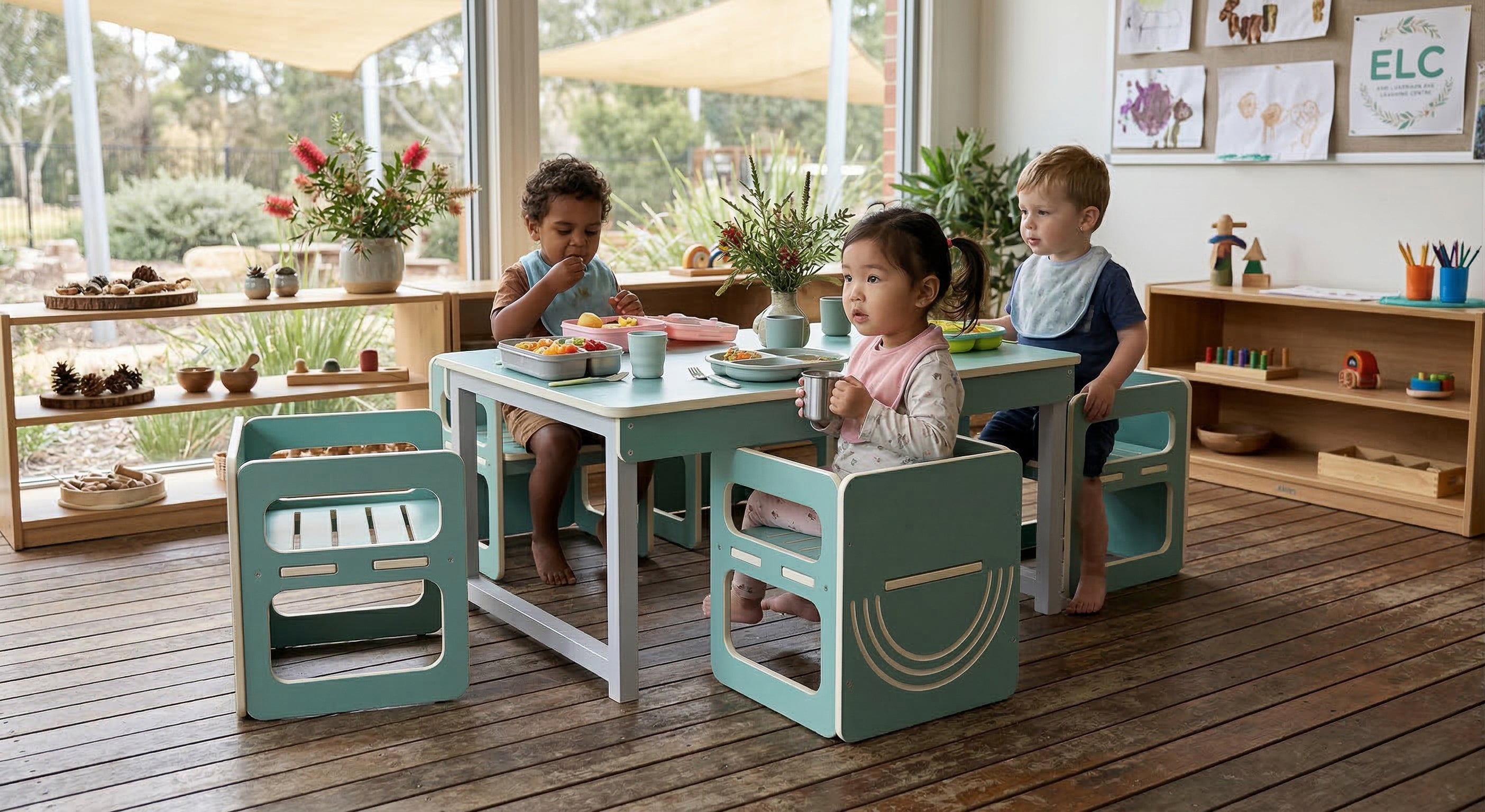 Children sitting at a table in a classroom setting with educational materials and plants.